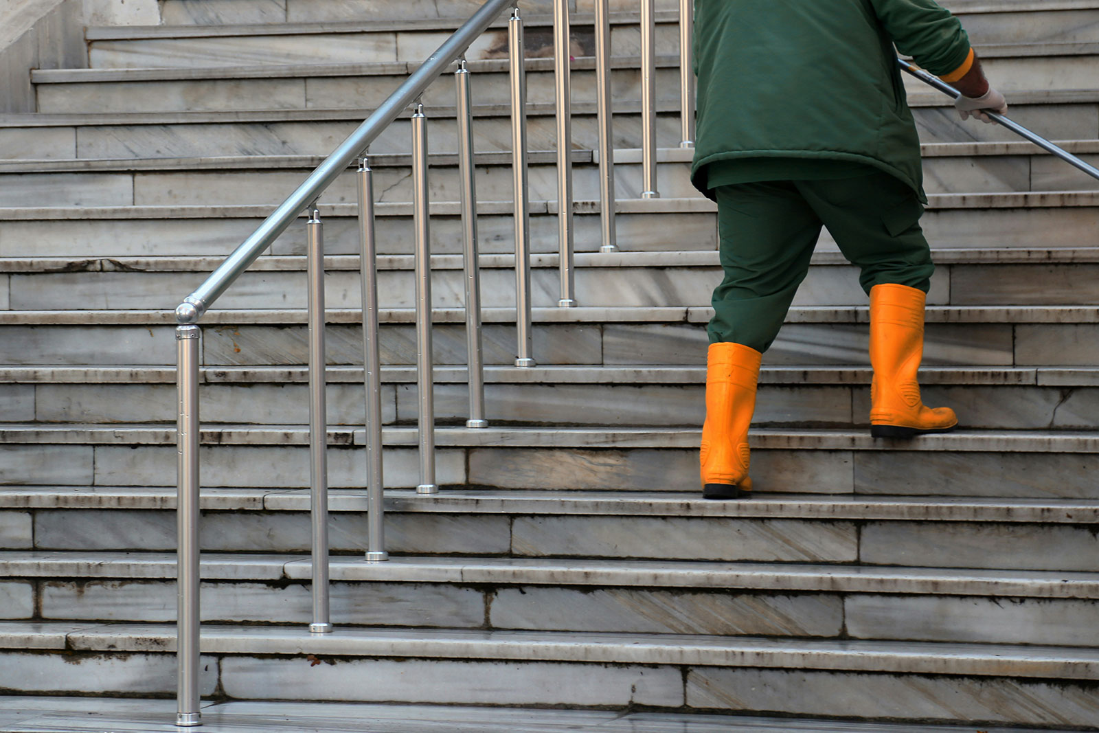 Ein Mann in einer grünen Jacke und orangen Gummistiefeln reinigt eine Treppe in Köln.